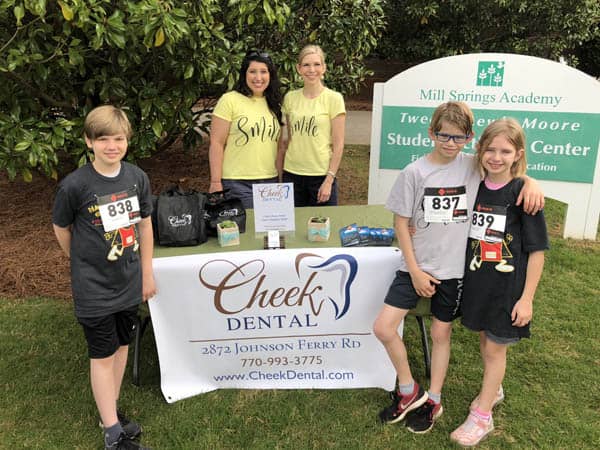 Outdoors photo of Dr. Kristi Chandler and Dr. Crisit Cheek behind a display table at the for the Nacho Ordinary 5k. Dr. Cheek's three children are in the forefront of the photo on either side of the table.