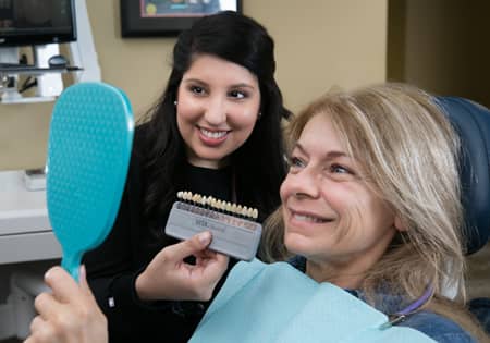Photo of East Cobb cosmetic dentist Dr. Chandler with a patient who might be interested in an alternative to Zoom whitening. The patient is looking in a mirror and Dr. Chandler is to her right holding a tooth shade chart.